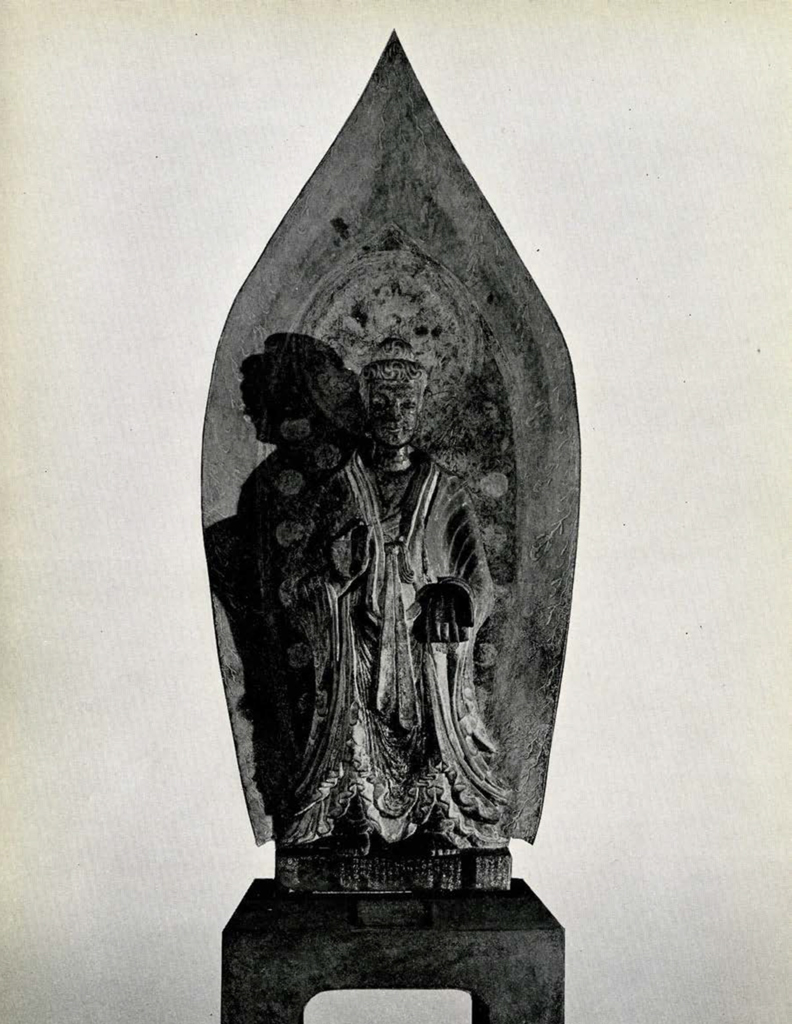 Life size statue in extremely high relief of Maitreya against a great leaf-shaped aureole with flame border and two small attendant bodhisattva figures
