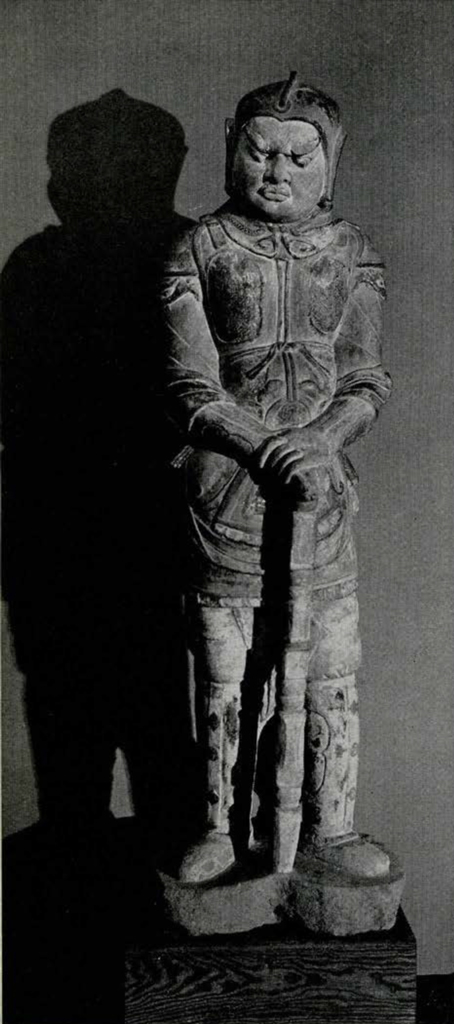 Carved stone statue of a lokapala leaning on a staff or sword, wearing a smooth headpiece
