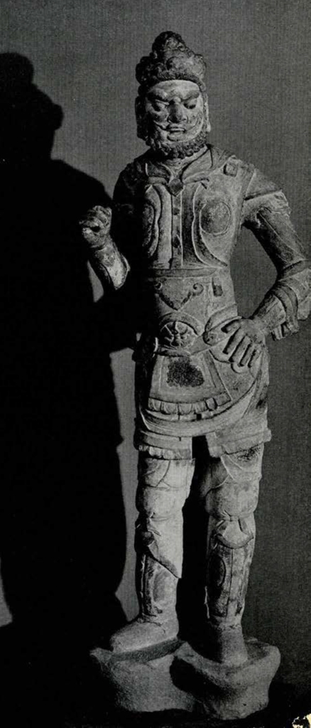 Carved stone statue of a lokapala, one hand on the hip, in Tang warrior uniform, curly beard