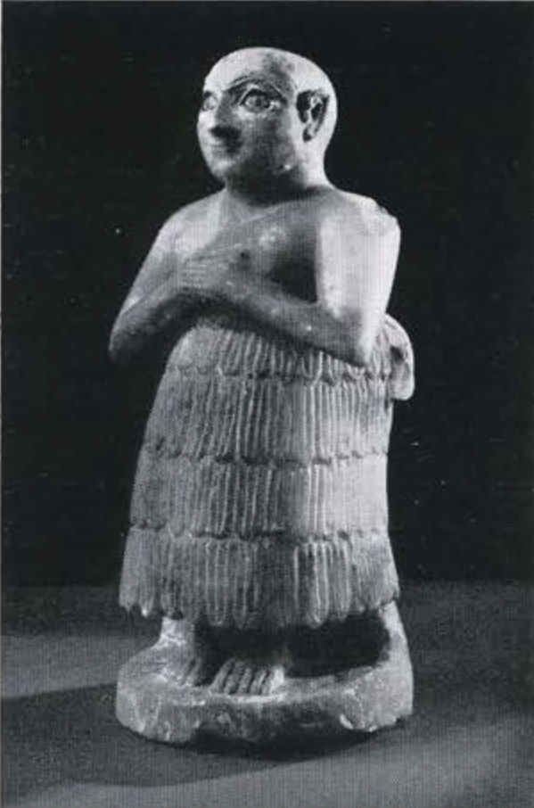 Statuette of a standing man in a tiered skirt, hands on his chest, bald