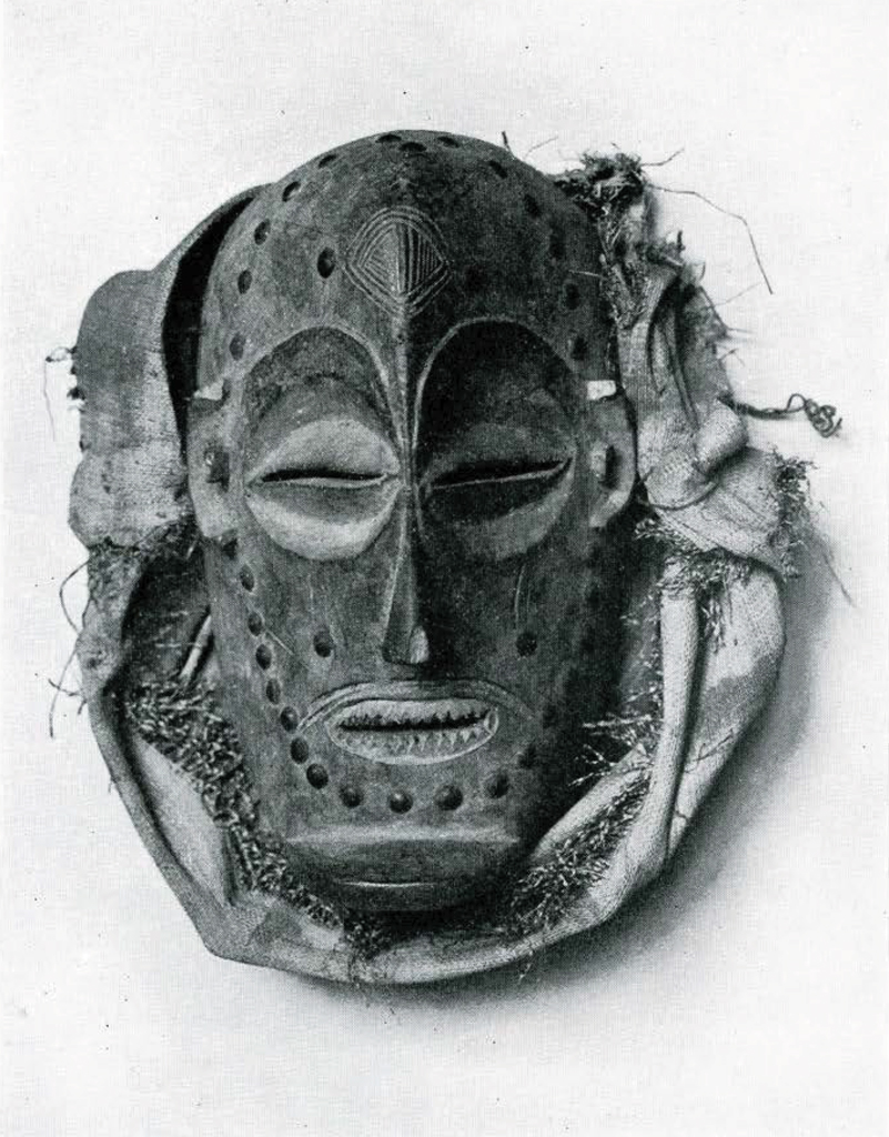 Wood dance mask with slits for eyes and mouth; sharp pointed teeth; prominent chin; incised lines (scarification?) on forehead and upper lip; studded with brass-headed nails.