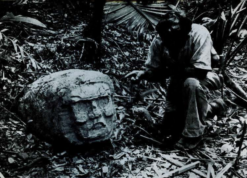 A man nealing next to a large stone carving of a head.