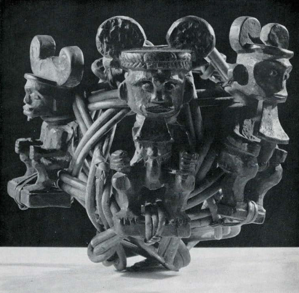 A woven ball with three wooden figurines attached to it, wearing headbands with circular protrusions.