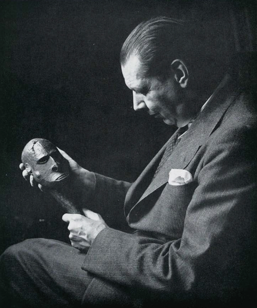 Rene D'Harnoncourt holding and examining a wooden flute stopper with the end carved into the shape of a head.