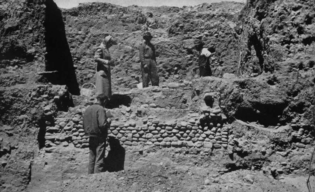 Three people standing on an excavated stone wall, in a trench.