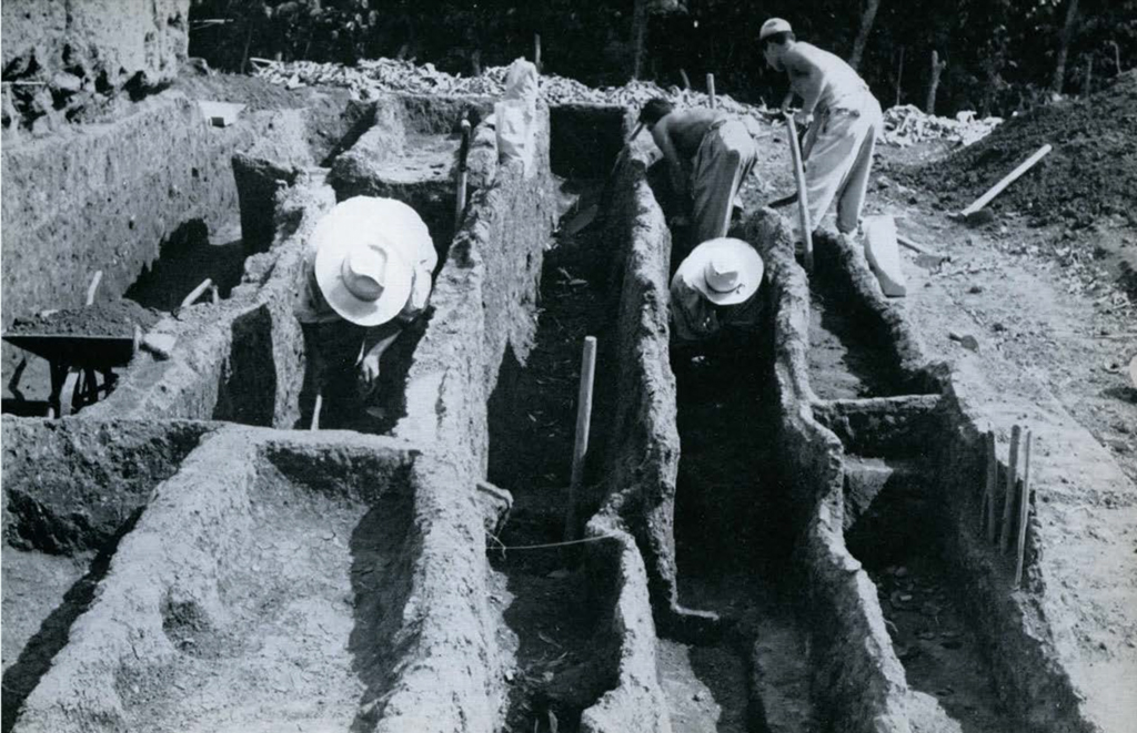 Four people digging out dirt from between clay walls.