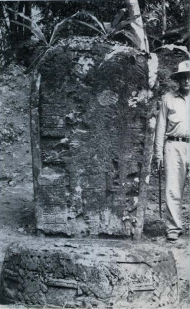 A man standing next to a large, carved stone stela that is the same height.