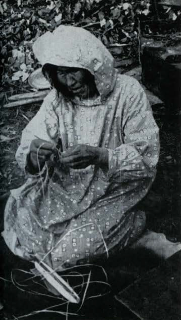 A woman kneeling on the ground, sewing a fishing net.
