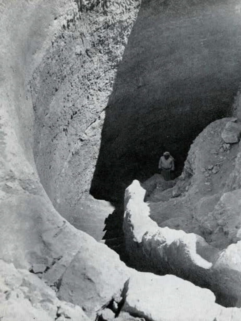 Looking down into a rock cut spiral staircase, a man stands at the bottom.