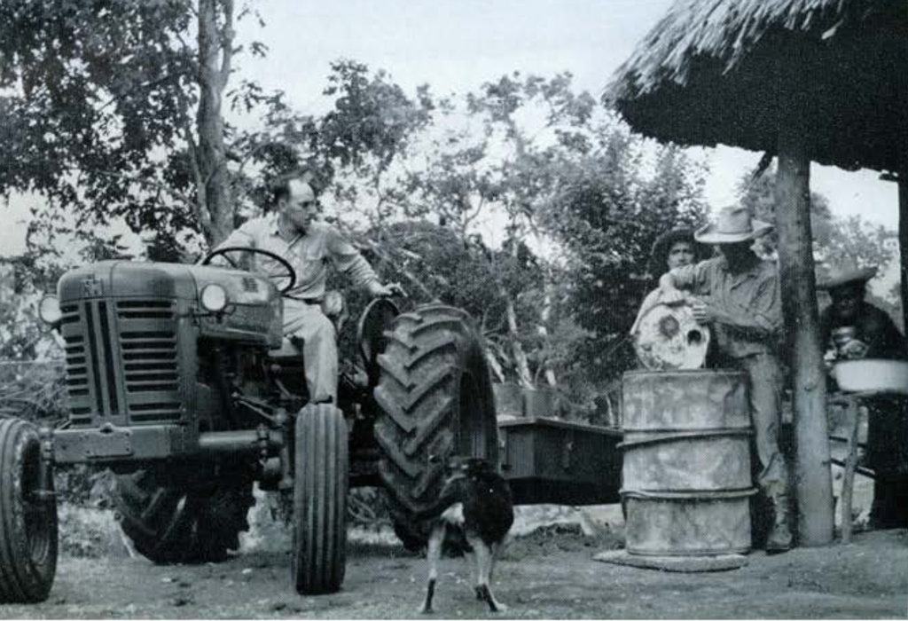 Men on tractors watching a man fill a barrel.