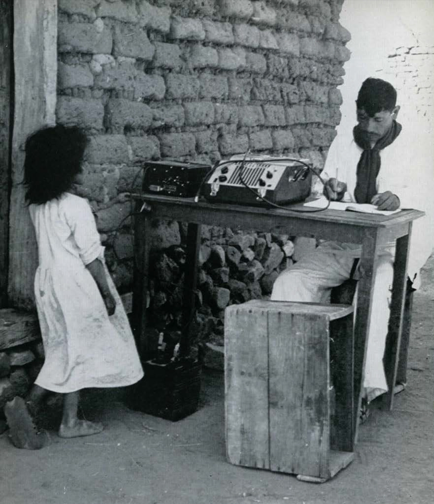 A man sitting at a desk with a recording aparatus, taking notes.