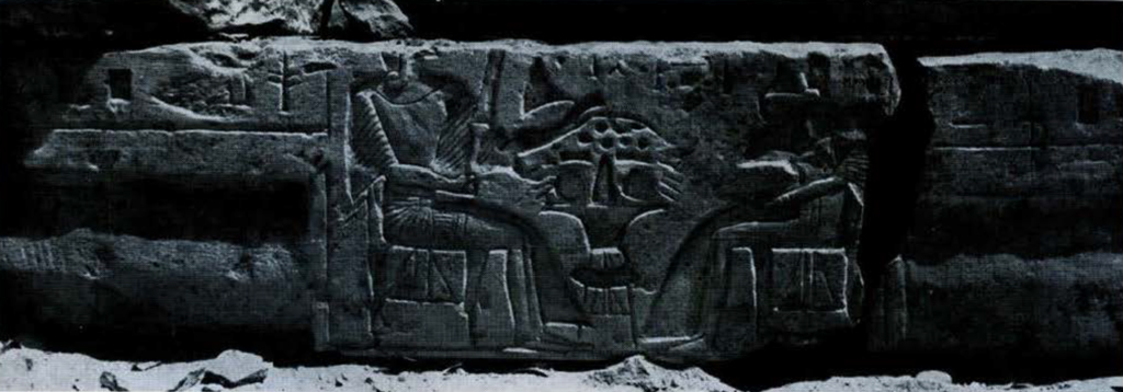 A lintel, cracked on one side, with carved depiction of two figures seated at a table.