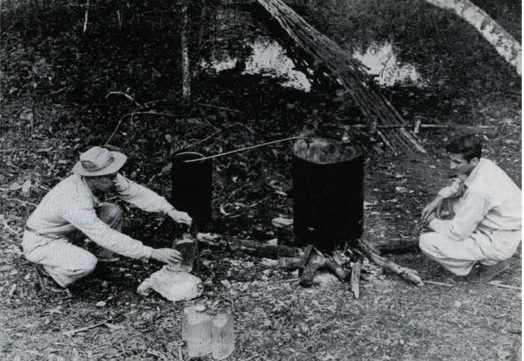 Two crouching men drawing water from a still and filling bottles.