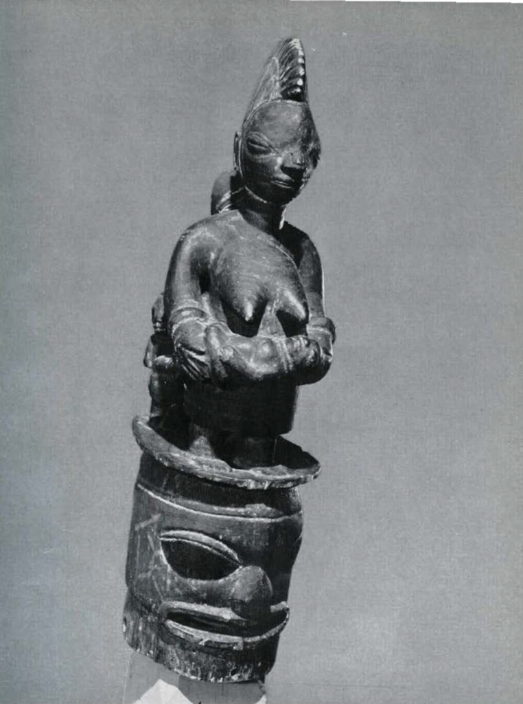 Wooden mask with a figure of a woman on top, the woman holding a child in her arms.
