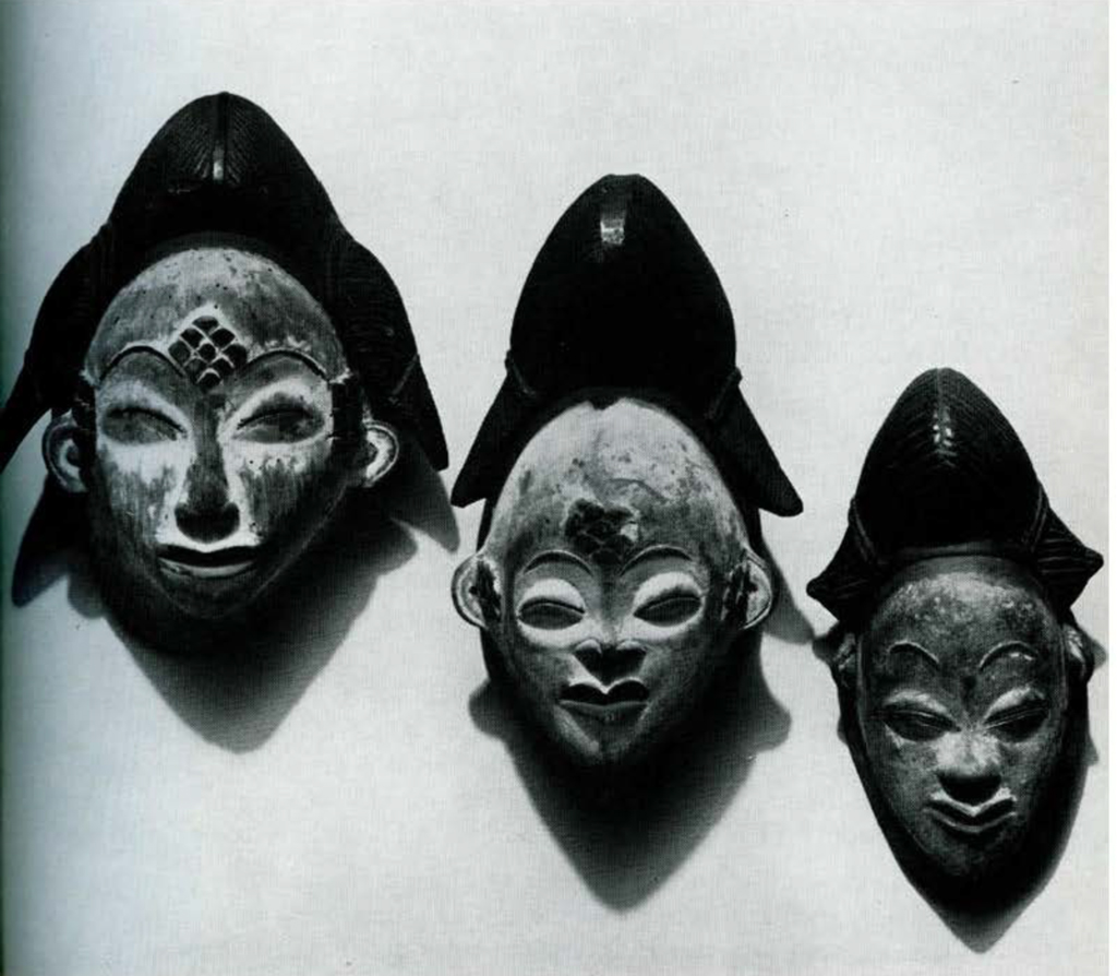 Three wooden masks with triangular head pieces, mounted on a wall.