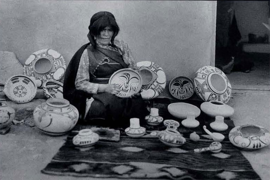 A woman seated on a blanket,the pottery she is selling placed around her.