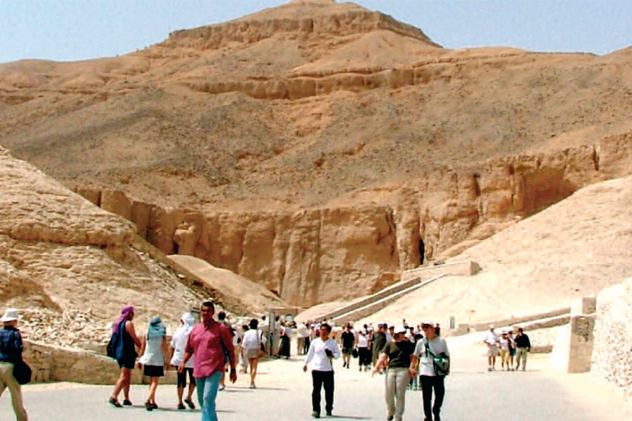 A crowd of people walking the path into the Valley of the Kings, a cliff peak rising above them in the distance.
