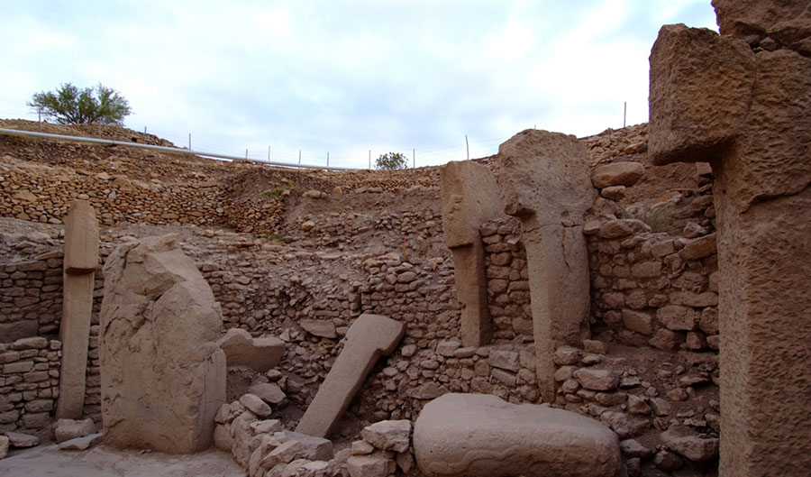 Excavated stone walls with massive stone pillars embedded into the walls and leaning against them.
