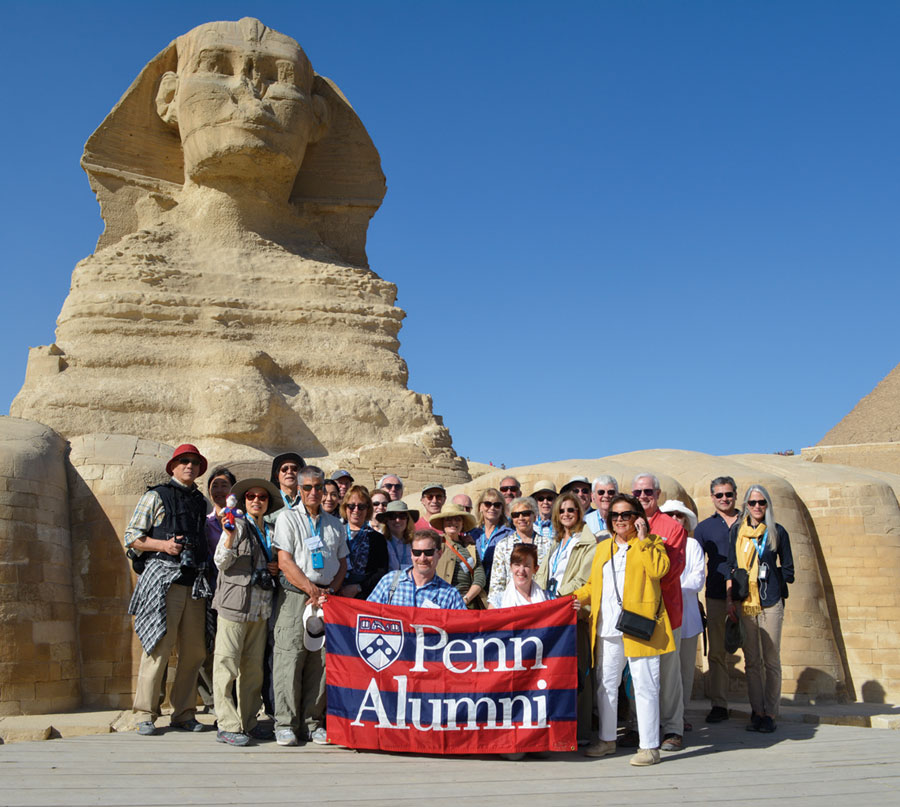A large group tour in front of the Sphinx holding a flag that says Penn Alumni