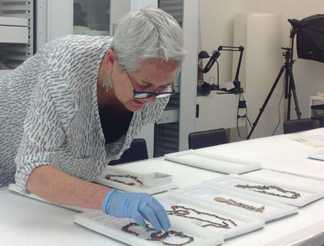 Jane Hickman examining jewelry in a lab while wearing surgical gloves.