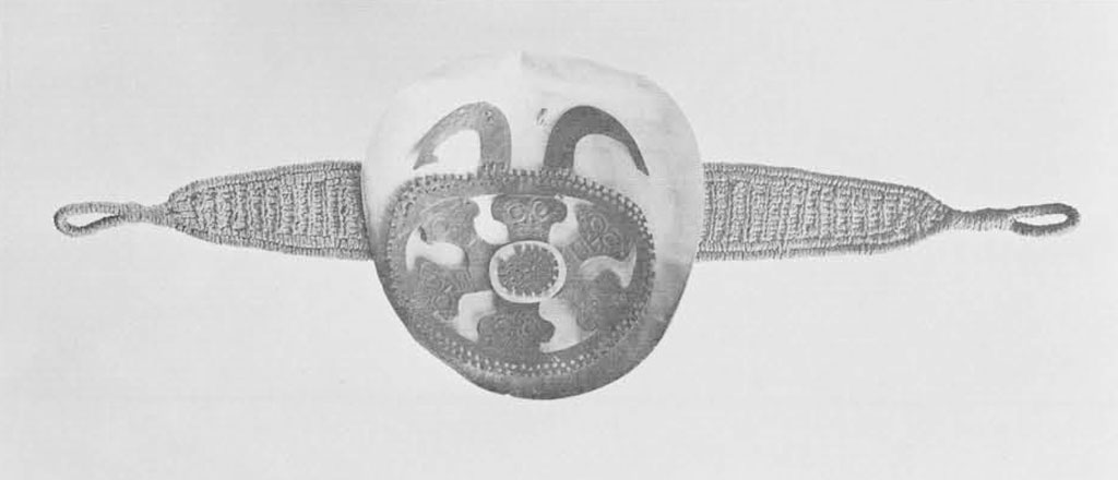 Headband of woven coconut fiber to which is attached a large disk of pearl shell overlaid with a carved sheet of sea turtle shell. The openwork carving includes six human faces and, at the top, two curved elements resembling the points of the large ceremonial fishhooks used to suspend sacrificial victims in temple areas.