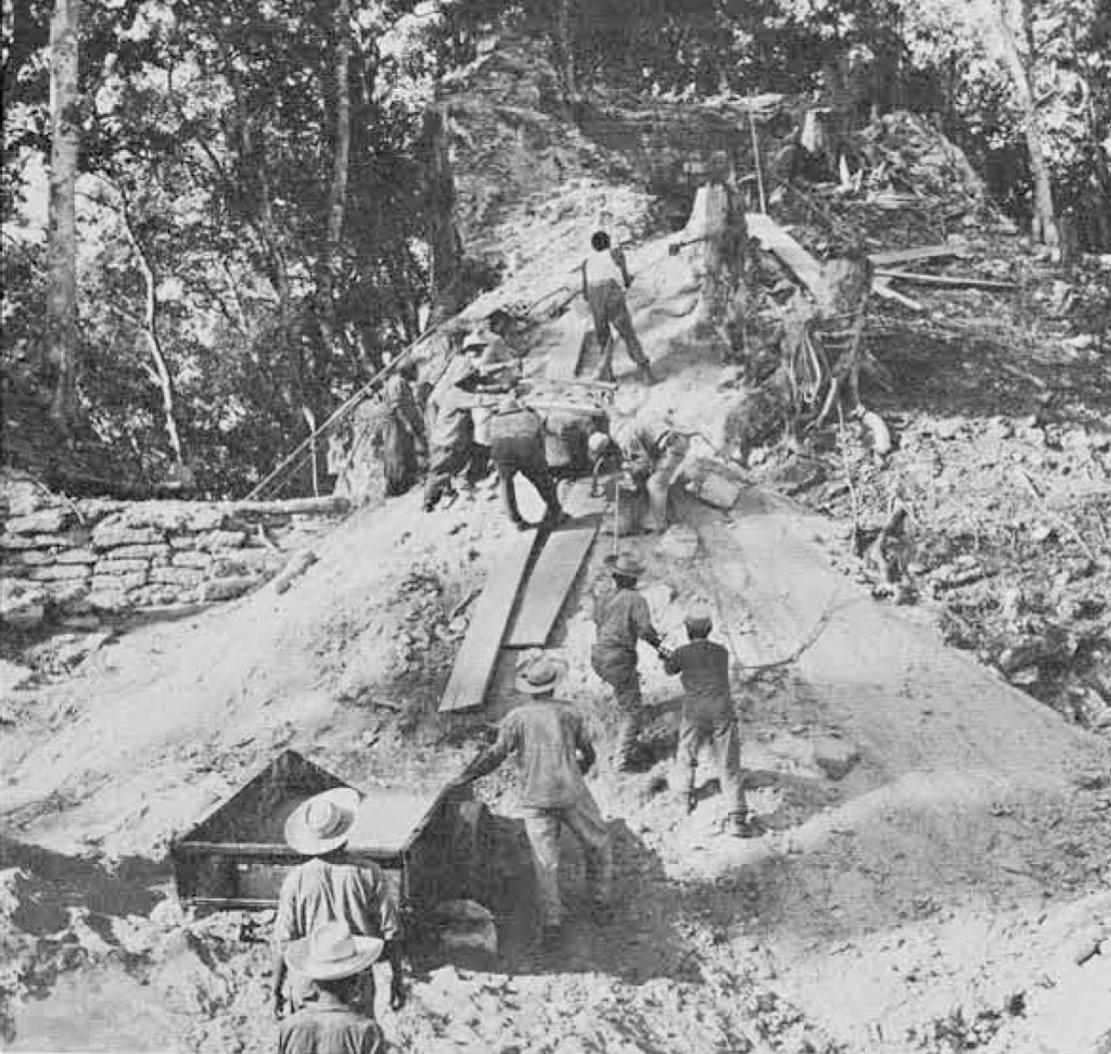 A team of people sliding a massive stone fragment down a dirt slope into a crate.