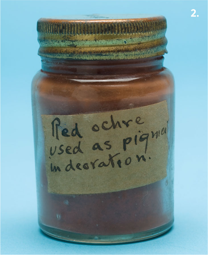 A glass jar filled with red powder with a label stating 'Red ochre used as pigment in decoration'.