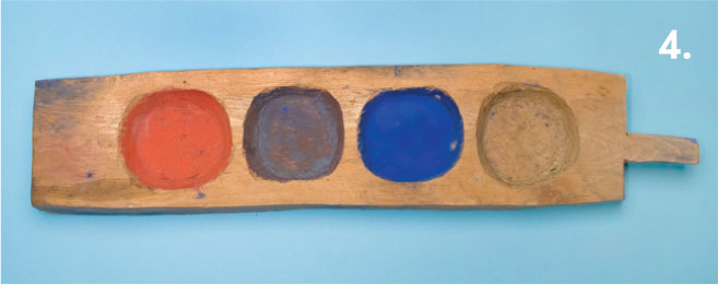 A piece of wood with four divots, each with a different color of paint.