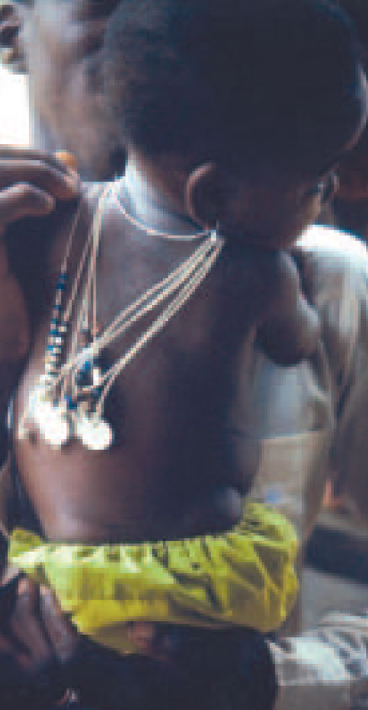 A baby with several necklaces that display shiny coins at the end hanging down its back.