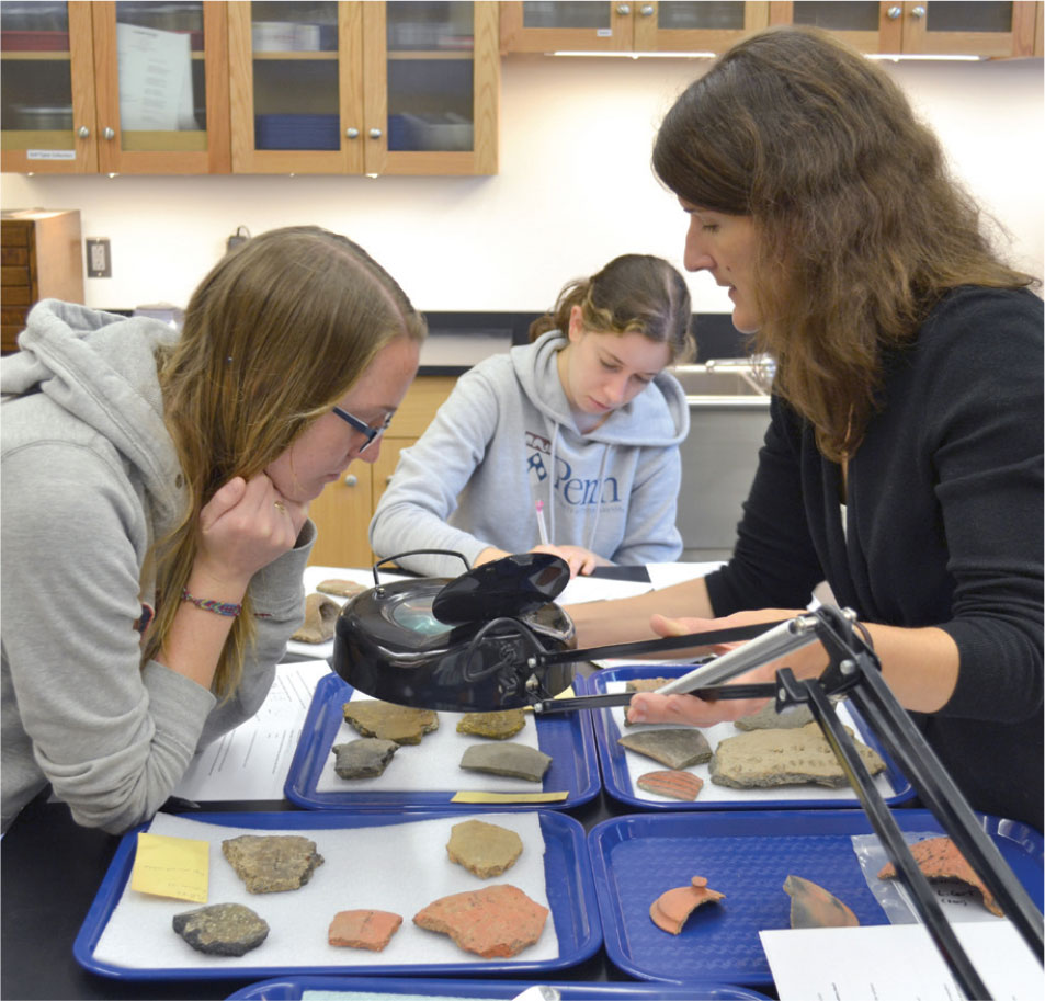 Marie-Claude showing two students ceramic pieces in a lab.