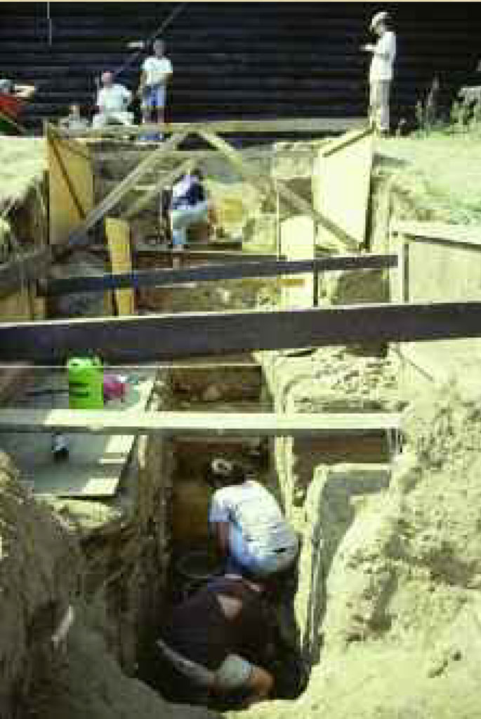 A team of people in an excavated trench with beams holding the sides of the trench up.