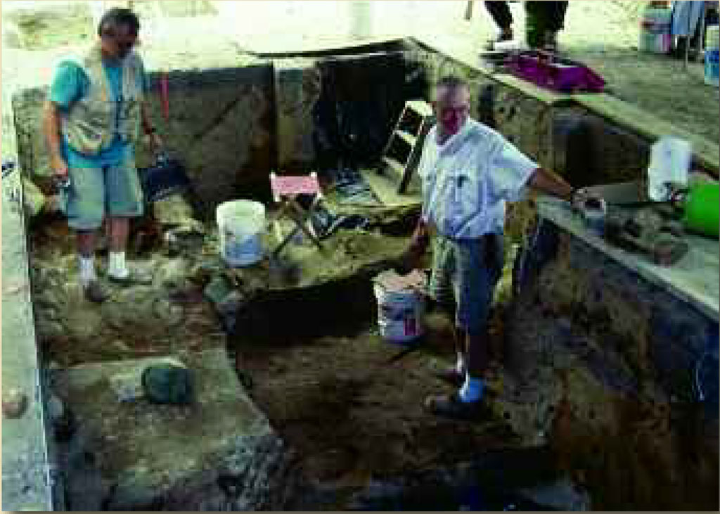 Two people in a rectangular area, with buckets filled with debris from the excavation.
