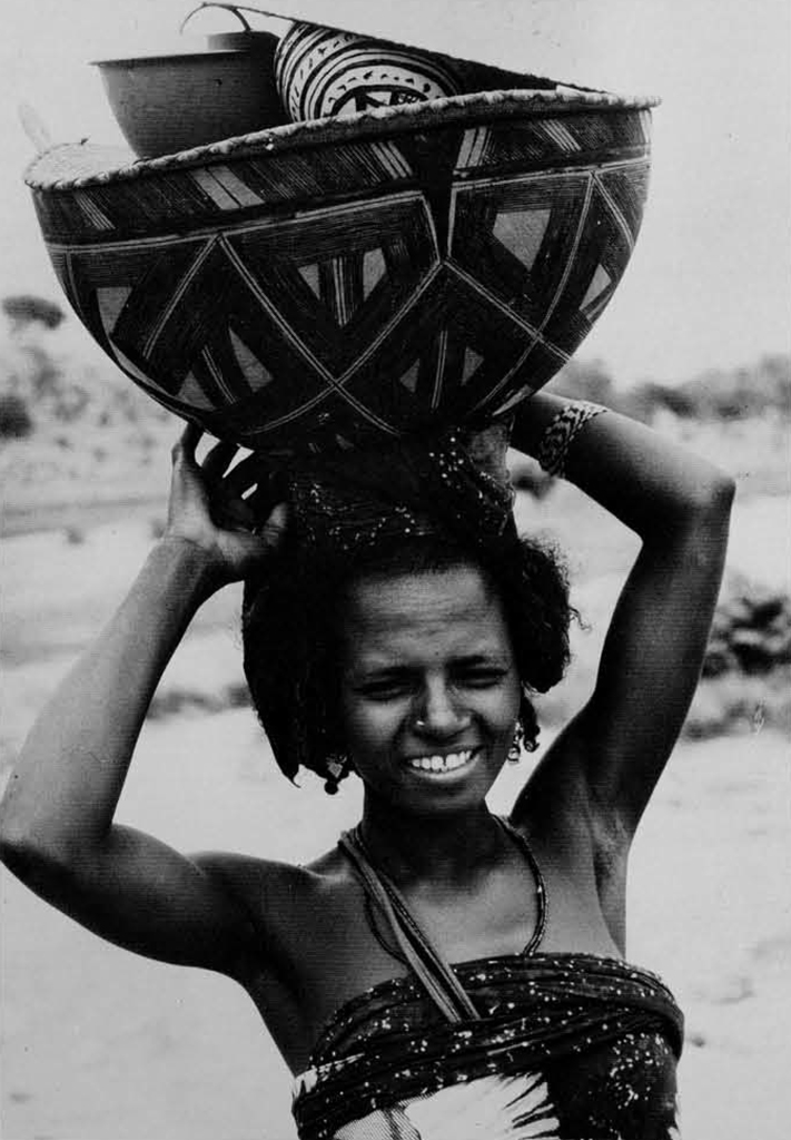 A woman carrying a massive calabash on her head.