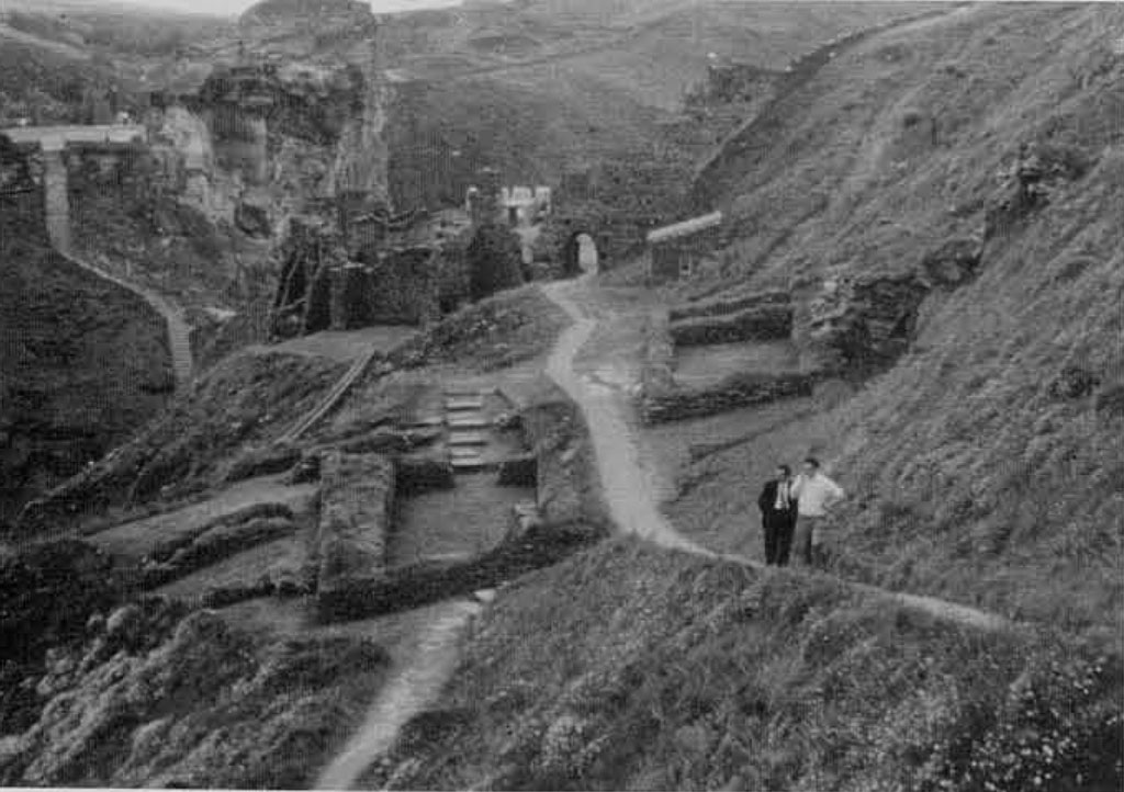 Two men walking a path through castle ruins on a hillside.