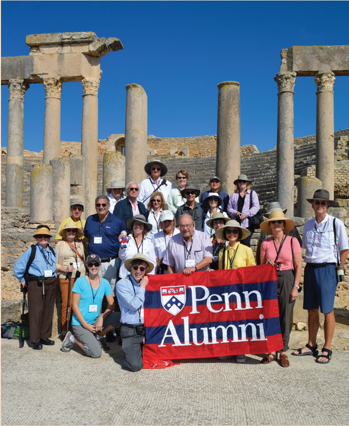 Penn Alumni in the ruins of Carthage, holding a Penn flag.