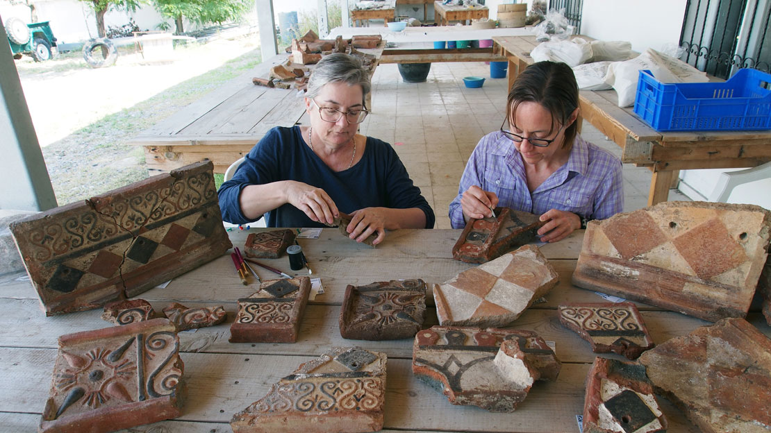 Two women working on pottery tiles with brushes to clean them.