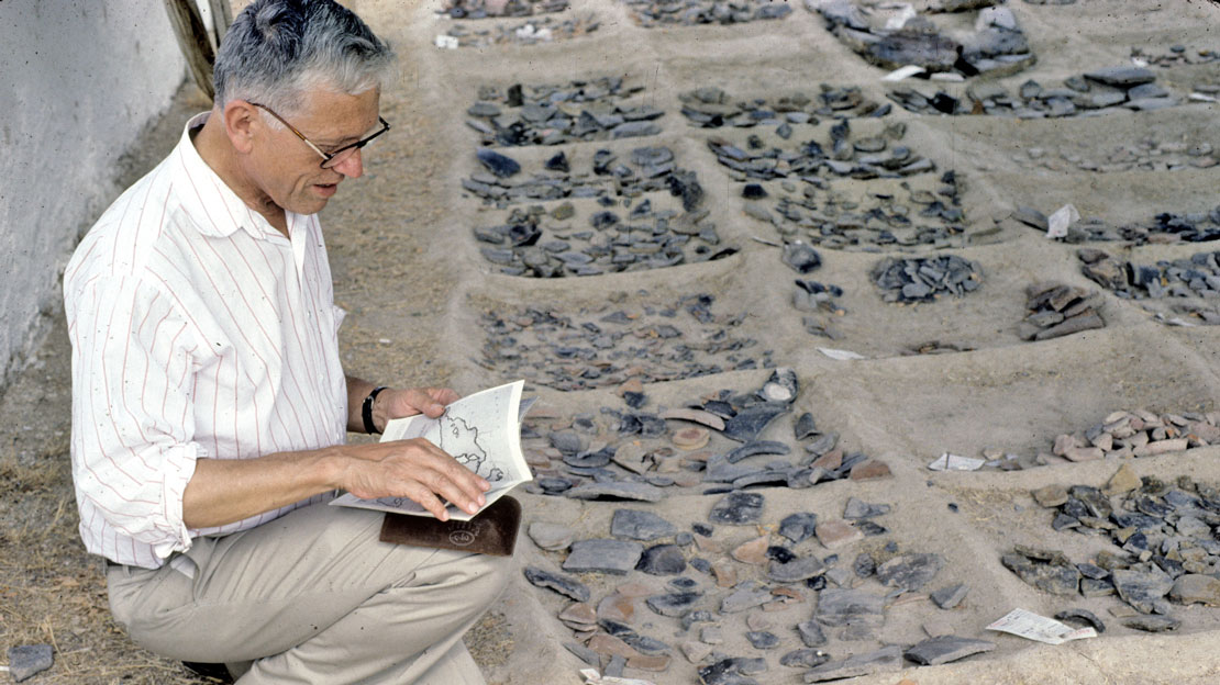 A man crouching next to a grid, each square of the grid filled with pottery sherds.