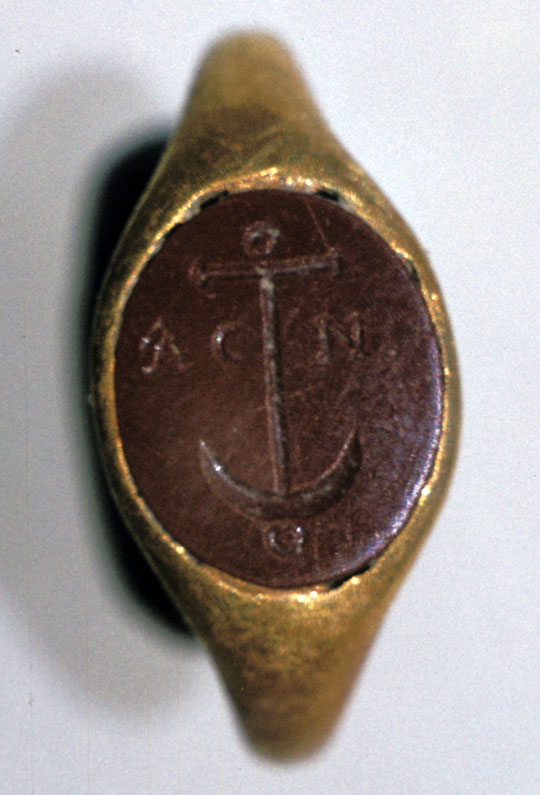 A gold ring with a red stone with an anchor carved into it.