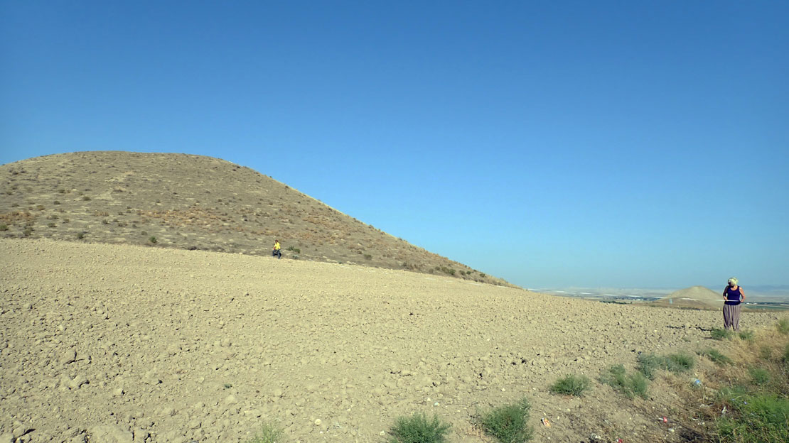 Two people surveying a rocky field in front of a massive mound.