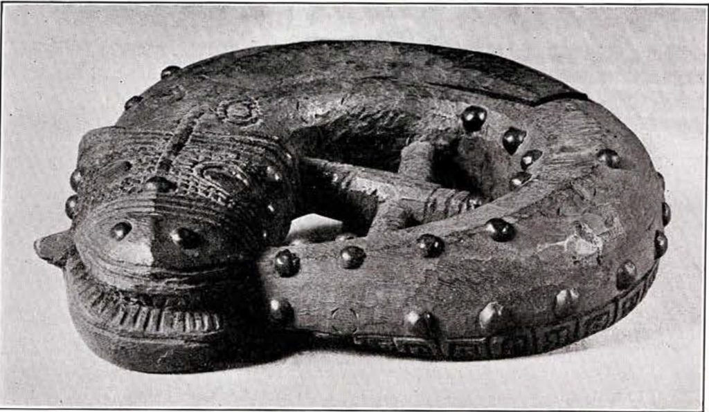 Carving of a fish in a circle biting its tail, with bumps and a cross bar in the middle