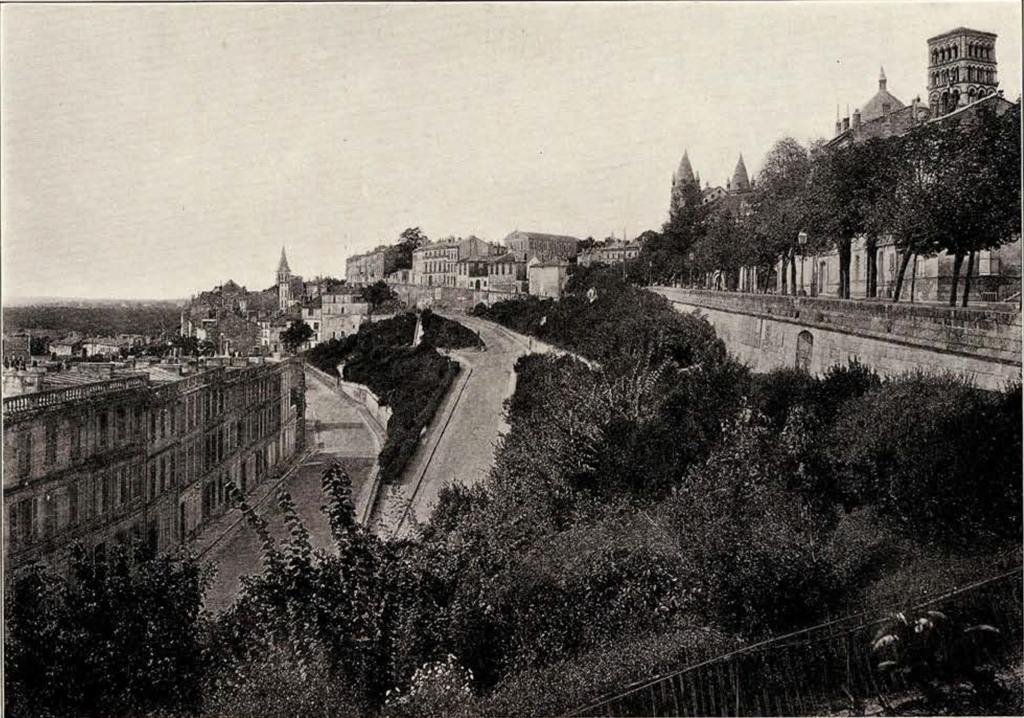 View of a village, with row house on the left, and a road zigzagging uptowards a large wall on the right