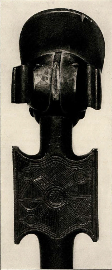 Head of a staff or baton showing a head wearing a tall curved headpiece, from the back