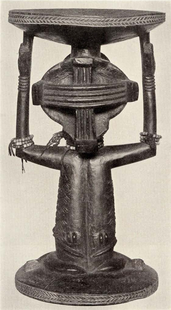 Wood carved stool, base is a seated woman wearing necklaces and bracelets using her arms and head to support the sitting area, back view showing designs in her hair