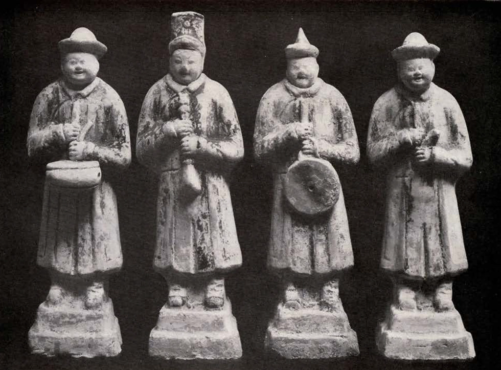 four figurines of standing men playing instruments each wearing a different hat but the same robes