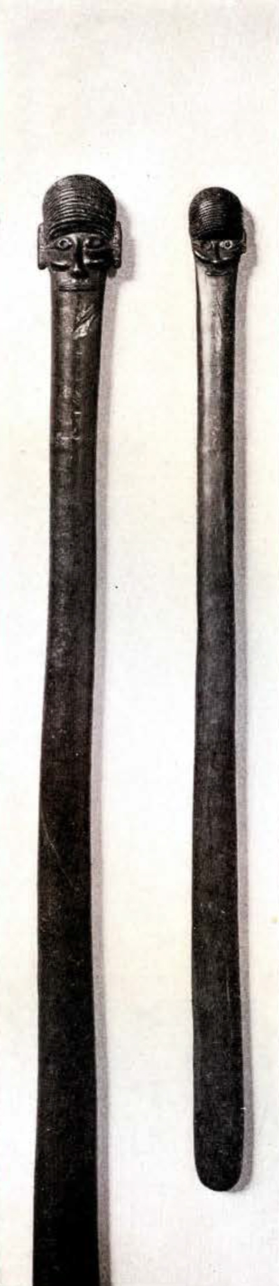 Two wooden staves, full length, one end of each carved into a head and face