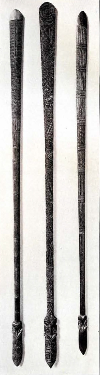 Three staves, full length, each with intricate carvings along the body and stylized faces at the blade