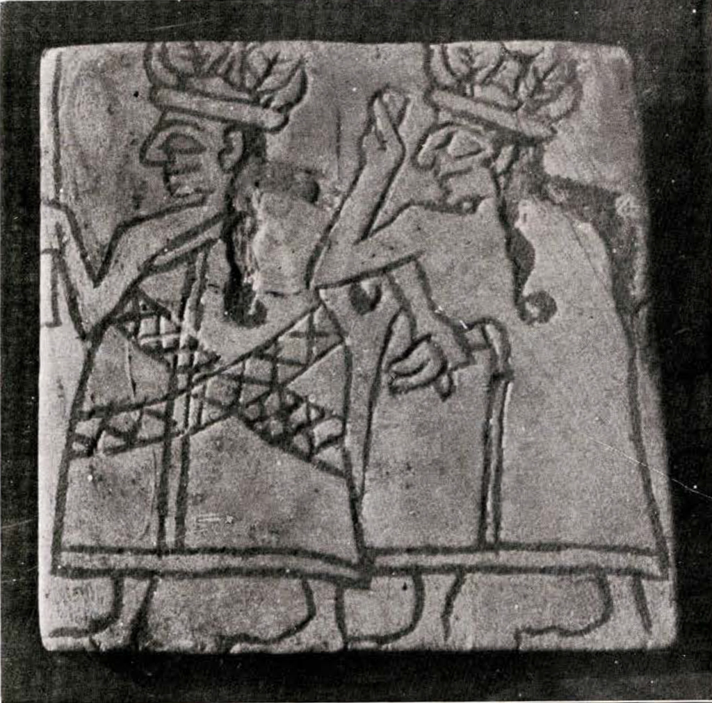 Square plaque with a carving of two figures wearing hats with long hair and garments, left figure has criss crosses on garment
