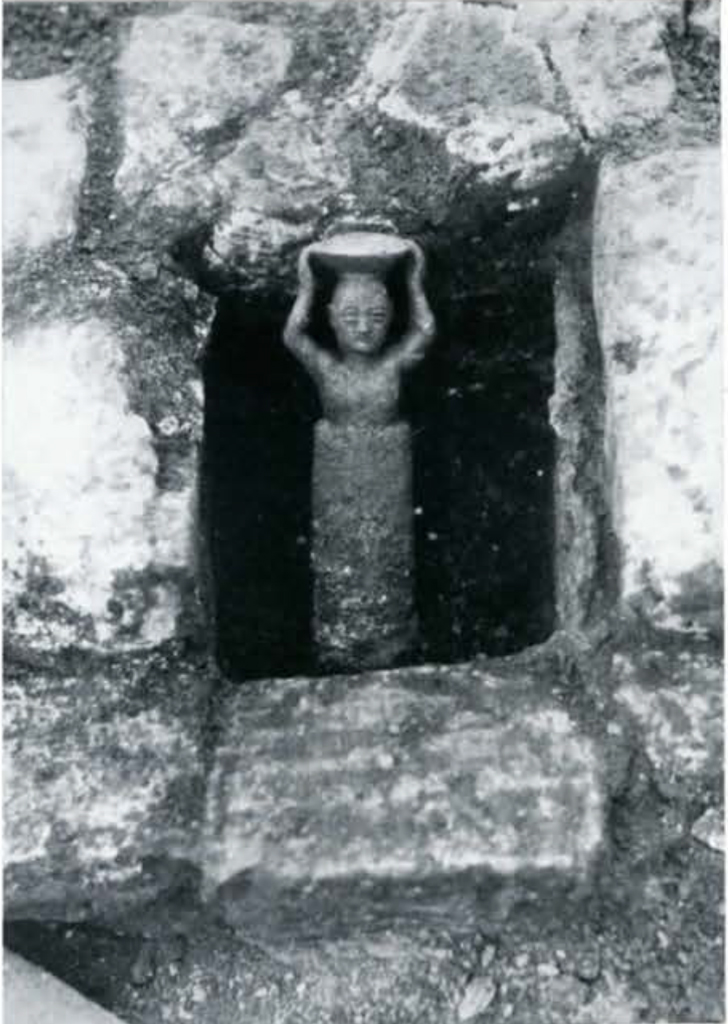 A small figure holding an object above its head, situated in an empty space in a wall or foundation