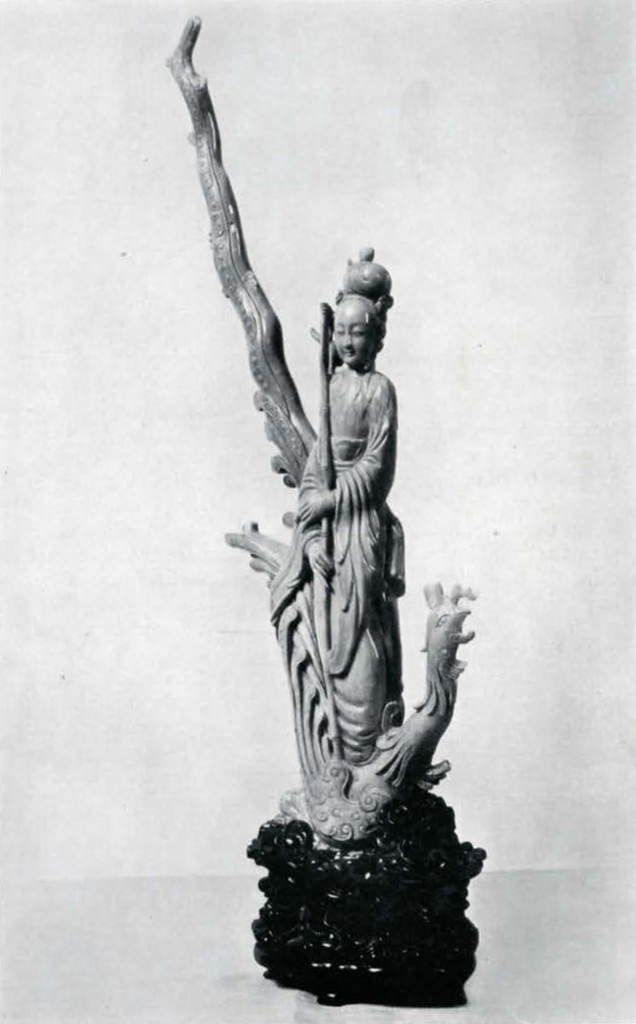 Figure of a female fairy standing on a dragon with a very long tail that extends vertically