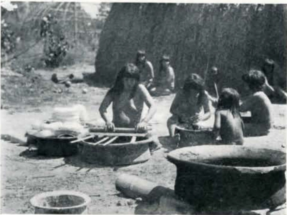 A group of women stiting on the group working over large pots